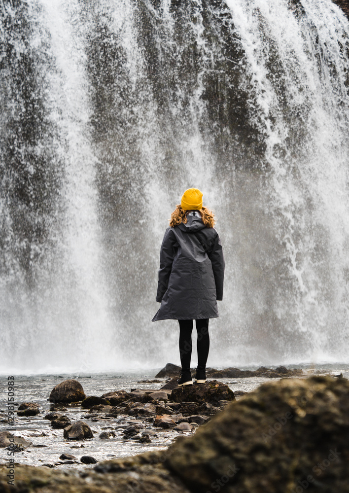 Woman in coat near waterfall Woman in coat near waterfall