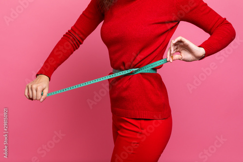 a girl in a red sweater and red pants measures her waist with a centimeter tape measure. the figure of a girl with a centimeter measuring the girl's waist