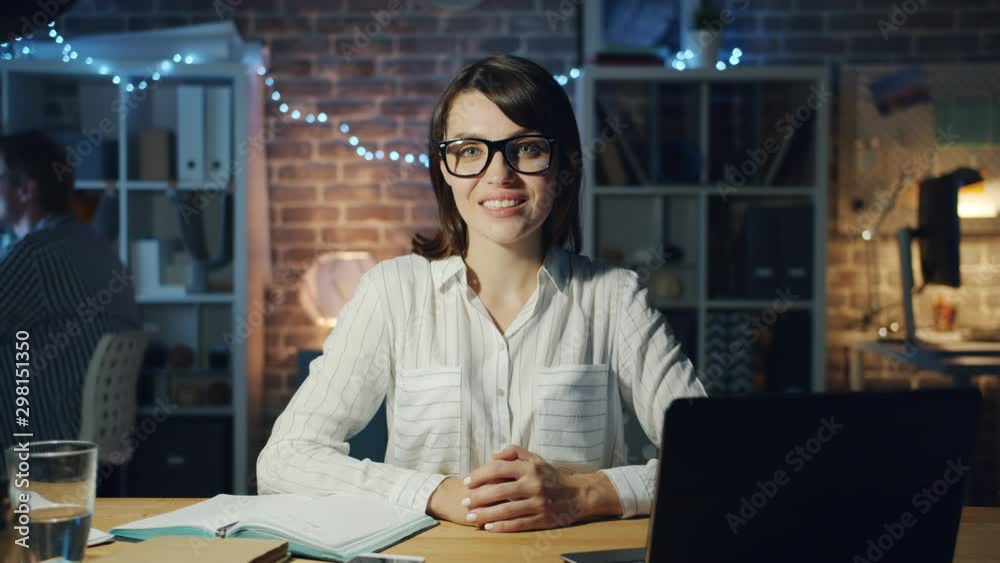 Slow motion of beautiful business lady smiling in office at night sitting at desk looking at camera. Workplace, successful career and emotions concept. Slow motion of beautiful business lady smiling in office at night sitting at desk looking at camera. Workplace, successful career and emotions concept.