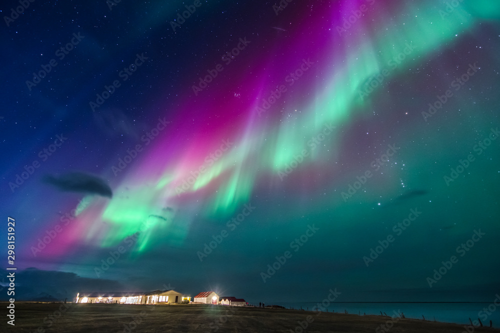 colorful northern lights on a iceland beach with cottages