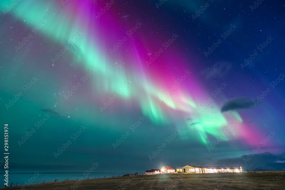 colorful northern lights on a iceland beach with cottages