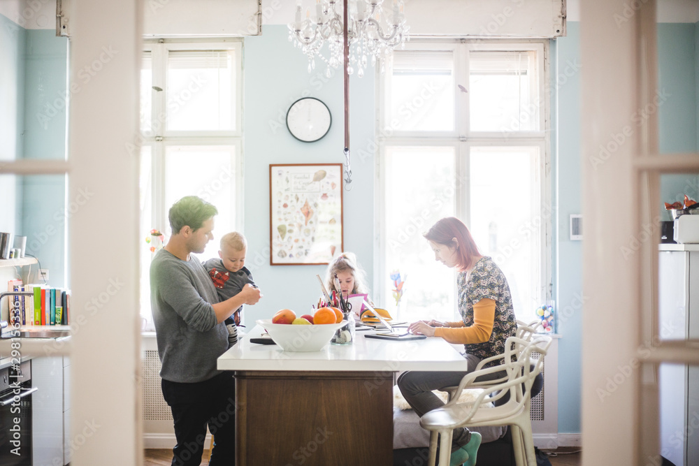 Father playing with son while standing by girl and woman busy at kitchen island Father playing with son while standing by girl and woman busy at kitchen island