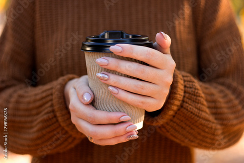 Hand holding warm coffee colorful leaves top view. woman holding tee cup drink to go autumn fall season