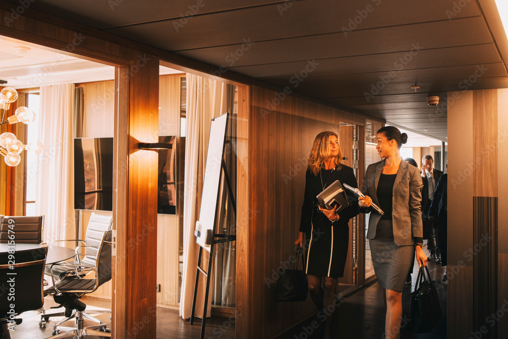Female lawyers talking while walking in corridor at law office Female lawyers talking while walking in corridor at law office