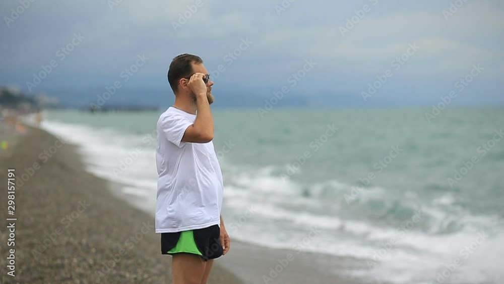 bearded man in sunglasses on the beach looking at the sea waves bearded man in sunglasses on the beach looking at the sea waves