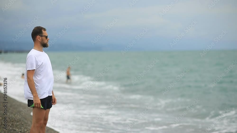 bearded man in sunglasses on the beach looking at the sea waves bearded man in sunglasses on the beach looking at the sea waves