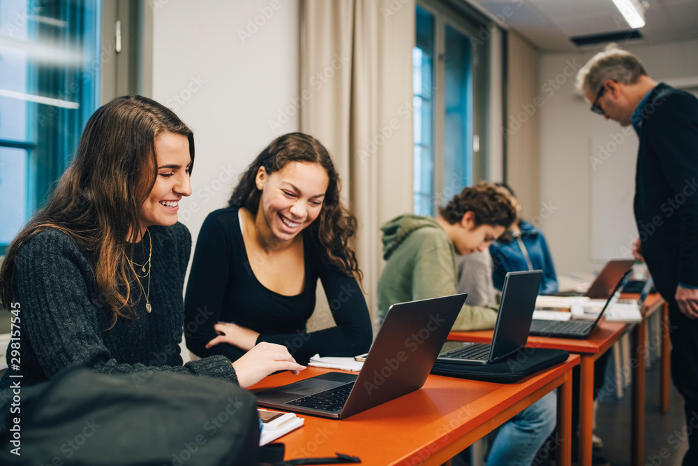 Cheerful female high school students using laptop at desk in classroom Cheerful female high school students using laptop at desk in classroom