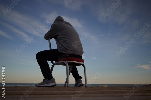 man sitting on a chair facing the sea concept of loneliness  depression and despair