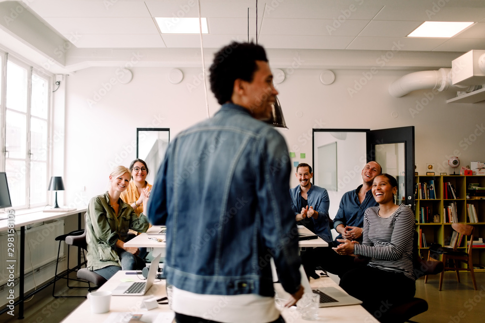 Rear view of smiling colleagues looking at businessman in office Rear view of smiling colleagues looking at businessman in office