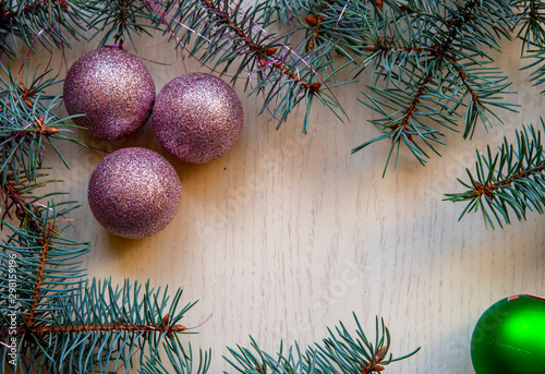 Branches of blue spruce and Christmas balls on a light wooden background.