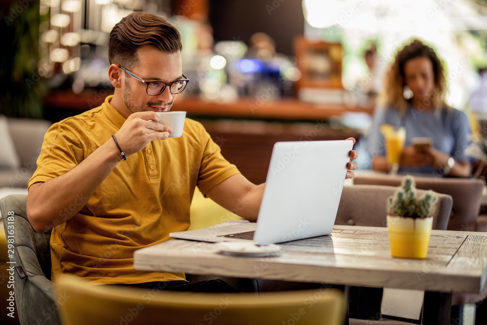 Young man drinking coffee while reading e-mail on a computer in a bar. Young man drinking coffee while reading e-mail on a computer in a bar.