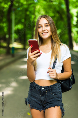 Happy young pretty woman outdoors in park using mobile phone.