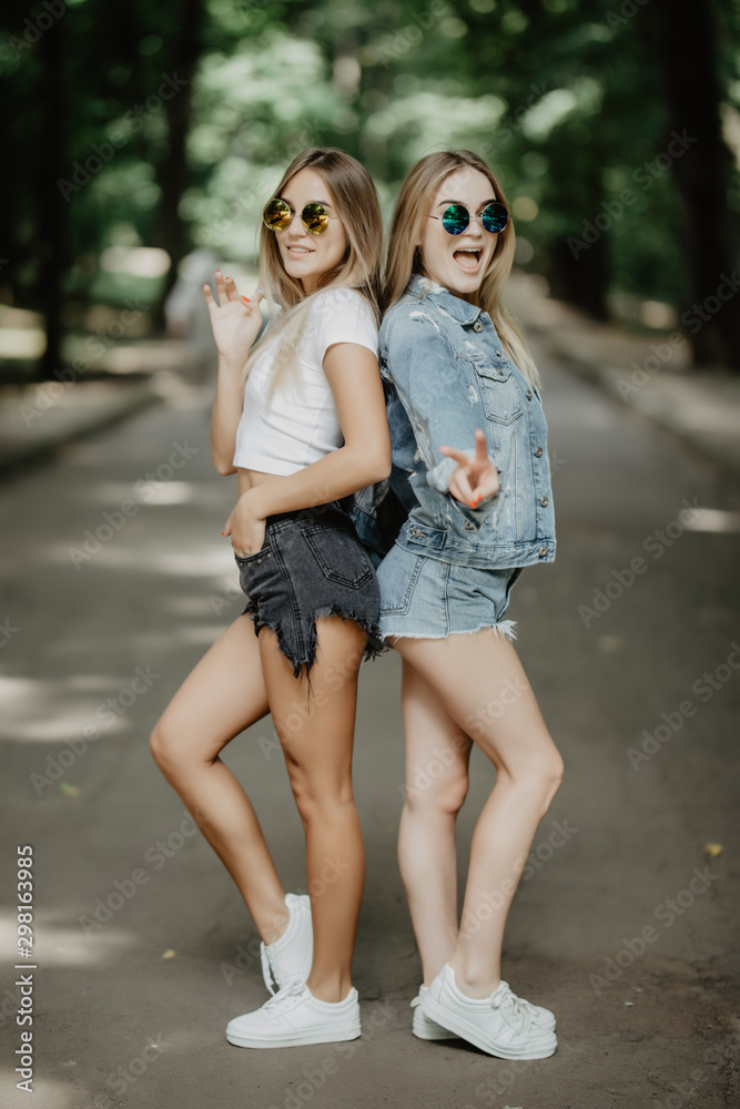 Two beautiful girls walking in the summer park have fun.