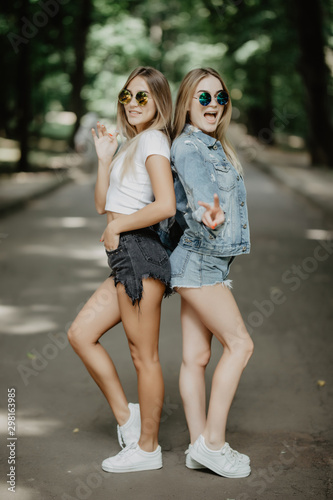 Two beautiful girls walking in the summer park have fun.