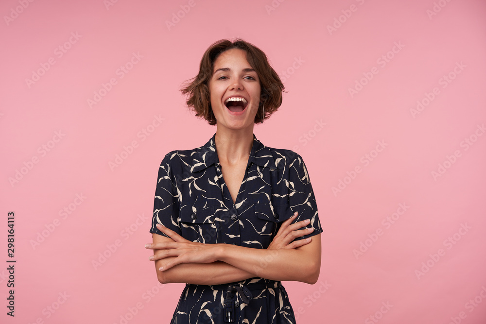 Indoor photo of joyful brunette female with casual hairstyle standing over pink background, keeping hands folded on her chest, looking at camera cheerfully with wide smile - obrazy, fototapety, plakaty 