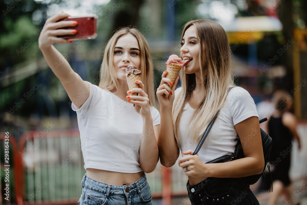 Portrait of two young women standing together eating ice cream and taking selfie in summer street. Portrait of two young women standing together eating ice cream and taking selfie in summer street.