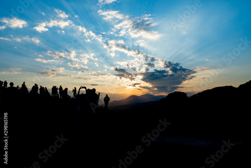 Silhouette of fo foreground hills and rocks of Meteora at sunset with crowd of tourists gathered to experience and photograph