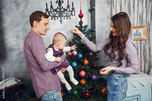 Cute family have fun in decorating room. Beautiful mother with little children and husband. Family near Christmas tree