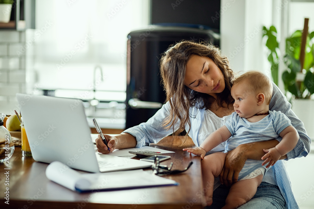 Young mother working on home finances and talking to her baby son. Young mother working on home finances and talking to her baby son.