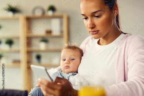 Young mother typing text message on mobile phone at home.