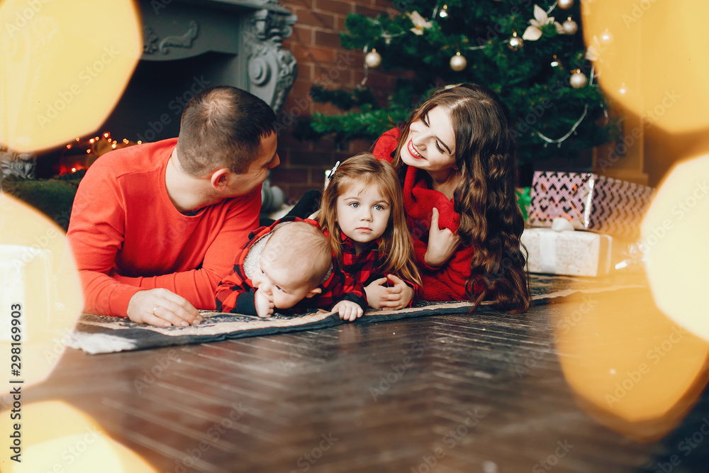 Fototapeta premium Beautiful mother in a red sweater. Family sitting near christmas gifts. Little girl and boy near christmas tree