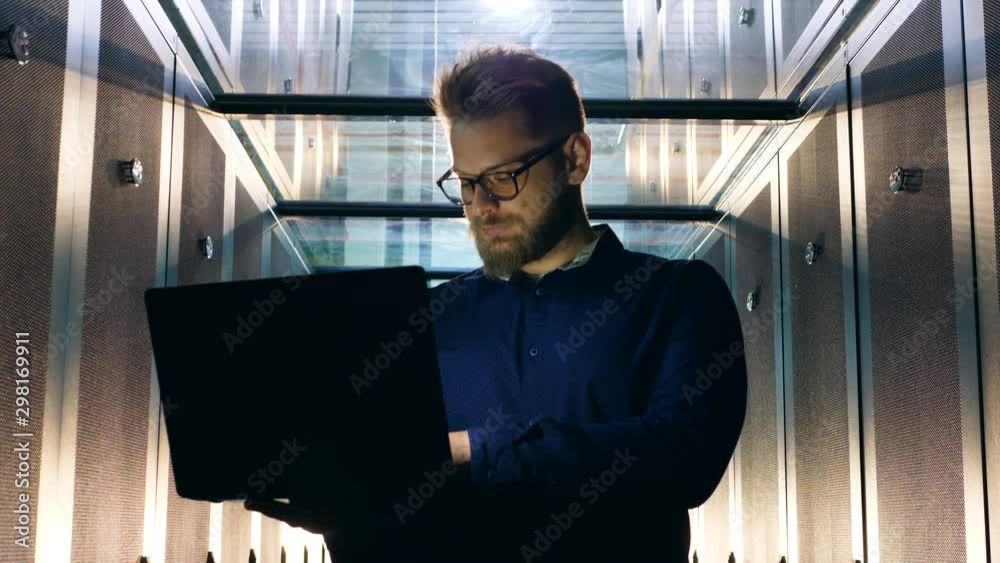 IT specialist types on laptop while working in server room.