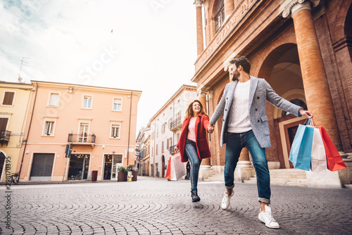 Canvas Print Young happy couple with shopping bags running in the city