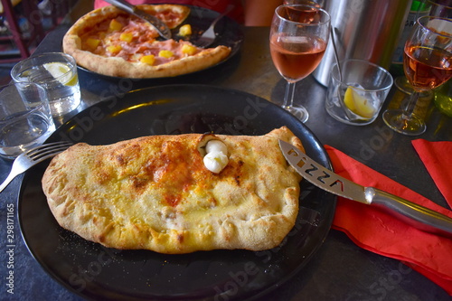 Parma ham and mozzarella cheese calzone which originated in Naples It is a traditional Italian oven baked folded pizza on the restaurant table accompanied by rose wine Hawaiian pizza in the background photo