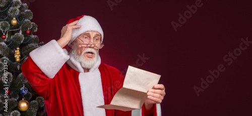 Santa Claus is reading the letters on the dark red background.