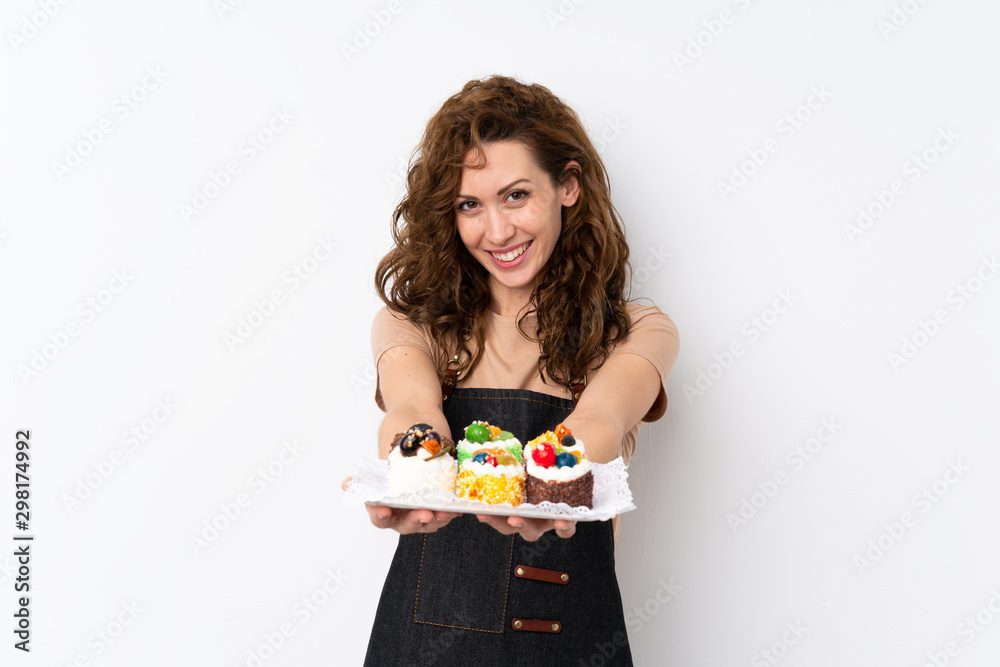 Young pretty woman over isolated background holding mini cakes Young pretty woman over isolated background holding mini cakes