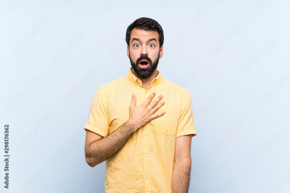 Naklejka premium Young man with beard over isolated blue background surprised and shocked while looking right
