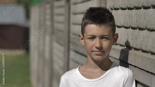 portrait of a funny boy outdoors near the fence stands and looks at the camera in the country photo