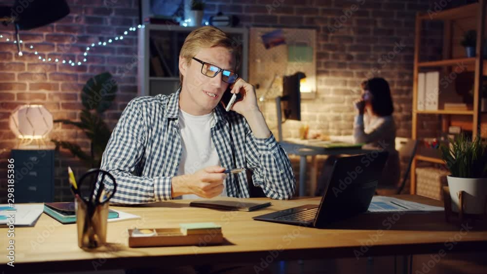 Angry businessman is speaking on mobile phone discussing business problems in dark office at night. Emotional people, work and communication concept. Angry businessman is speaking on mobile phone discussing business problems in dark office at night. Emotional people, work and communication concept.