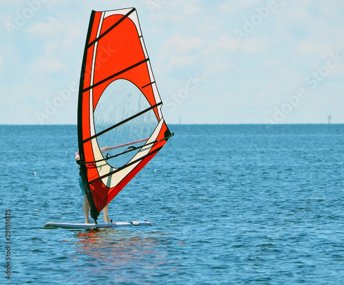 Windsurfer riding a board with a red sail