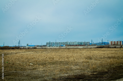 Photos Landscape on a field with dried grass and residential buildings in the distance