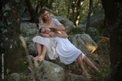 Woman in a forest sitting and relaxing with her daughter lying on her legs as the sun goes down