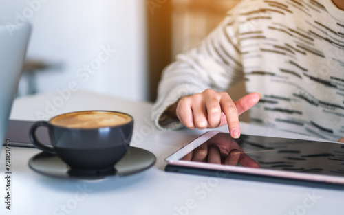 A woman using and pointing finger at a tablet pc with coffee cup on the table