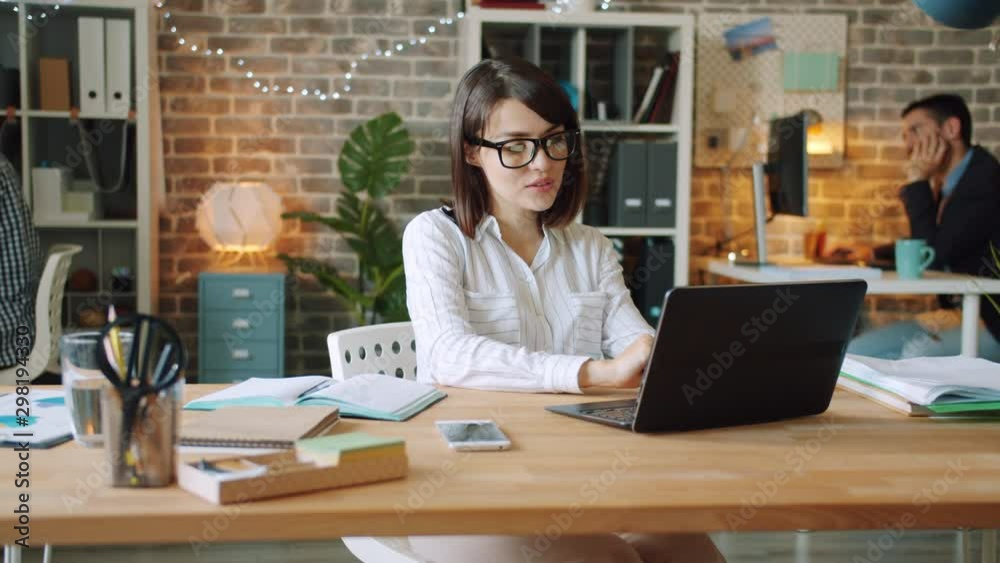 Happy businesswoman is working in office late at night using computer writing in notebook smiling enjoying work. People, workaholism and business concept.