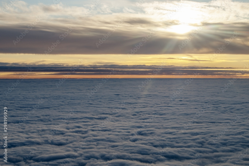 Field of fluffy clouds below going to the horizon. From above through clouds are rays of the sun. Picture from the window of the aircraft taken at an altitude of ten thousand meters during the dawn