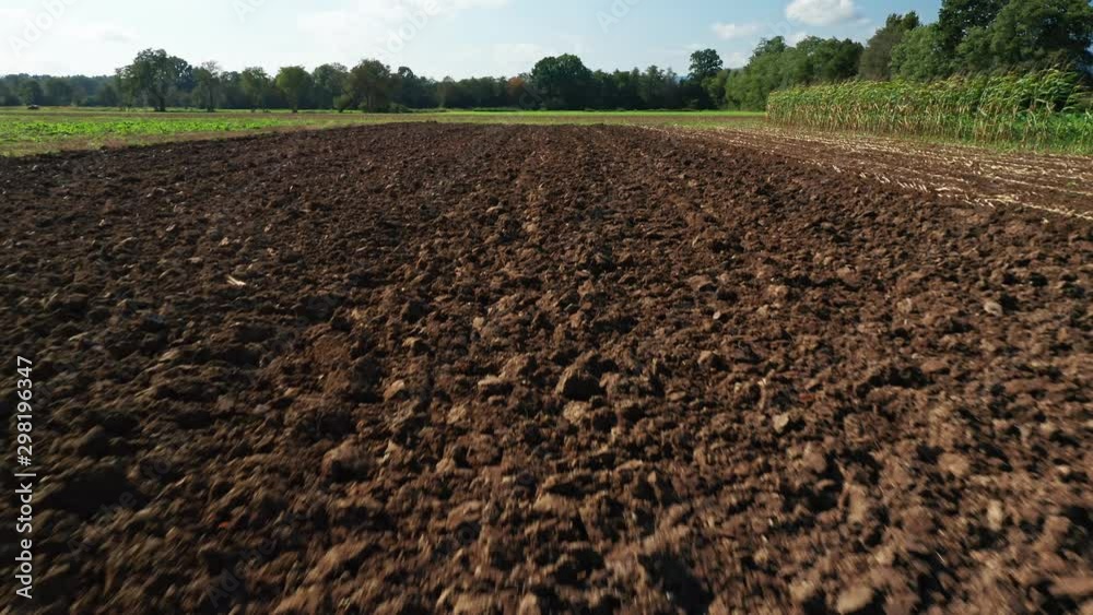 Ploughed field in autumn, flyover, hedges and trees in background, agiculture and cultivating soil concept
