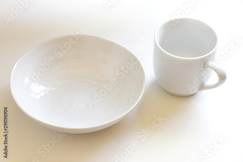 白いテーブルに置かれた何も入っていない白い皿とマグカップ