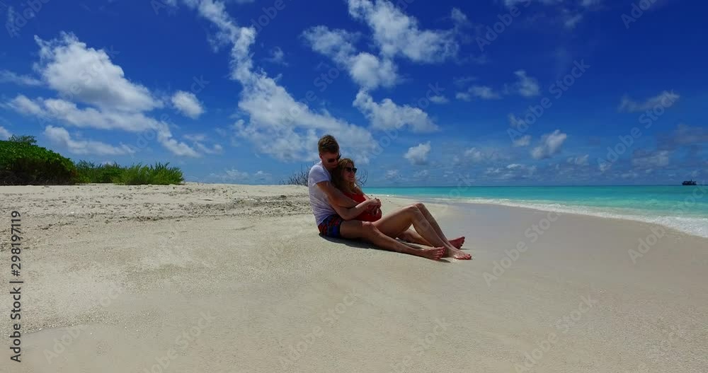 Lovely couple sitting on beach in Hawaii during honeymoon with waves gently breaking on their feet, white tshirt Lovely couple sitting on beach in Hawaii during honeymoon with waves gently breaking on their feet, white tshirt