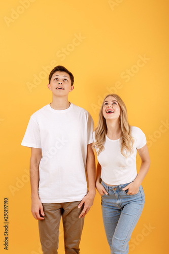 Happy emotional man and woman looking upwards at empty space, orange studio background