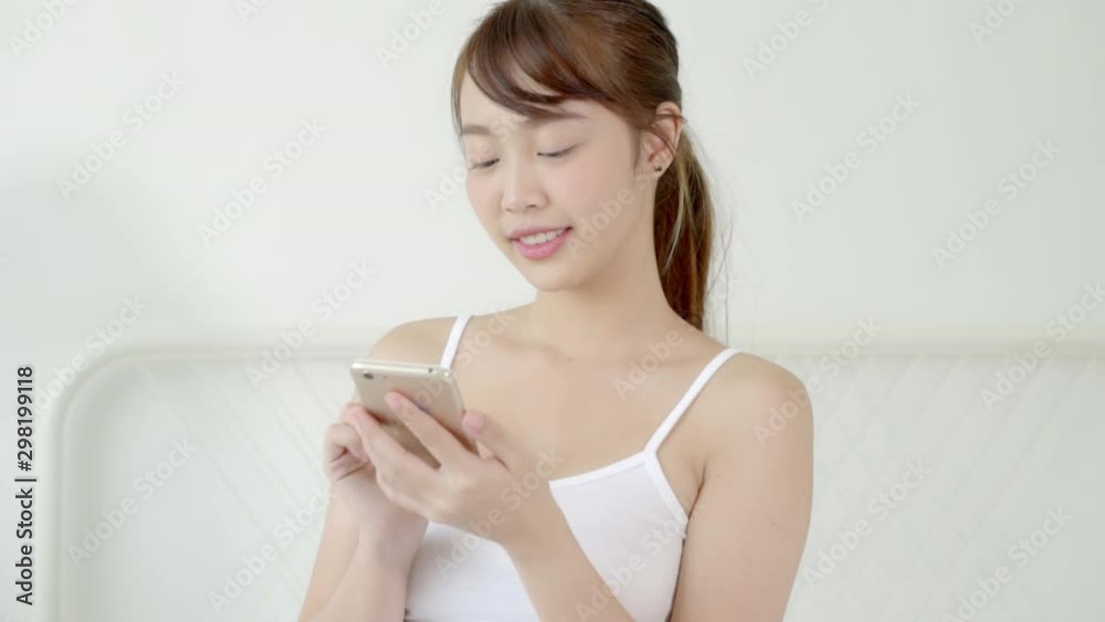 Beautiful portrait young asian woman smiling sitting look smart mobile phone reading social network with enjoy on bed at bedroom, girl chat messaging to internet online, communication concept. Beautiful portrait young asian woman smiling sitting look smart mobile phone reading social network with enjoy on bed at bedroom, girl chat messaging to internet online, communication concept.