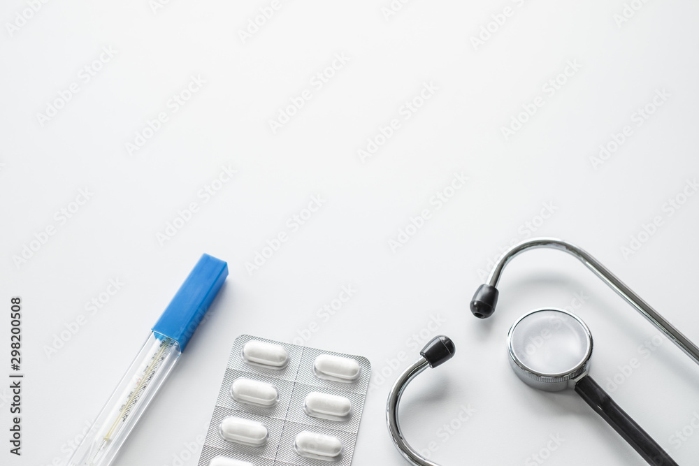 A stethoscope and thermometers and pills on white background A stethoscope and thermometers and pills on white background