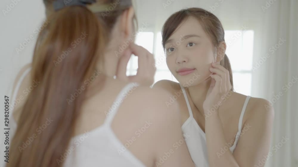 Beauty portrait young asian woman smiling look at mirror of checking skin care caucasian with wellness in the bedroom, beautiful girl happy touching face in reflection for health, lifestyle concept. Beauty portrait young asian woman smiling look at mirror of checking skin care caucasian with wellness in the bedroom, beautiful girl happy touching face in reflection for health, lifestyle concept.