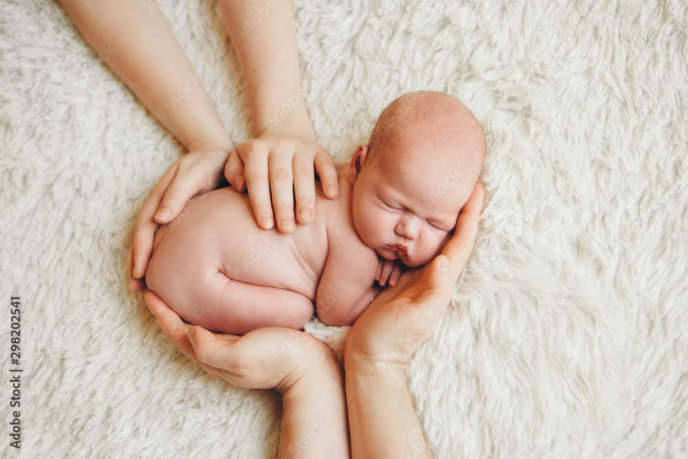 naked newborn baby lying on the hands of parents on a white background. Imitation of a baby in the womb. beautiful little girl sleeping lying on her stomach. naked newborn baby lying on the hands of parents on a white background. Imitation of a baby in the womb. beautiful little girl sleeping lying on her stomach.