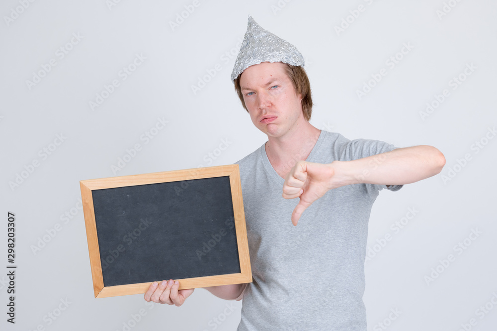 Sad young man with tin foil hat holding blackboard and giving thumbs down Sad young man with tin foil hat holding blackboard and giving thumbs down