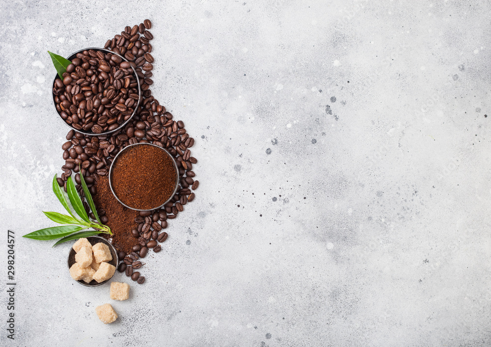 Fresh raw organic coffee beans with ground powder and cane sugar cubes with coffee trea leaf on light kitchen table background. Fresh raw organic coffee beans with ground powder and cane sugar cubes with coffee trea leaf on light kitchen table background.