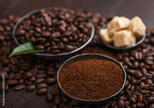 Fresh raw organic coffee beans with ground powder and cane sugar cubes with coffee trea leaf on brown background.